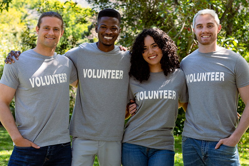 Group of smiling deverse female and male volunteers in matching tshirts looking at camera. eco conservation volunteers doing countryside clean-up.